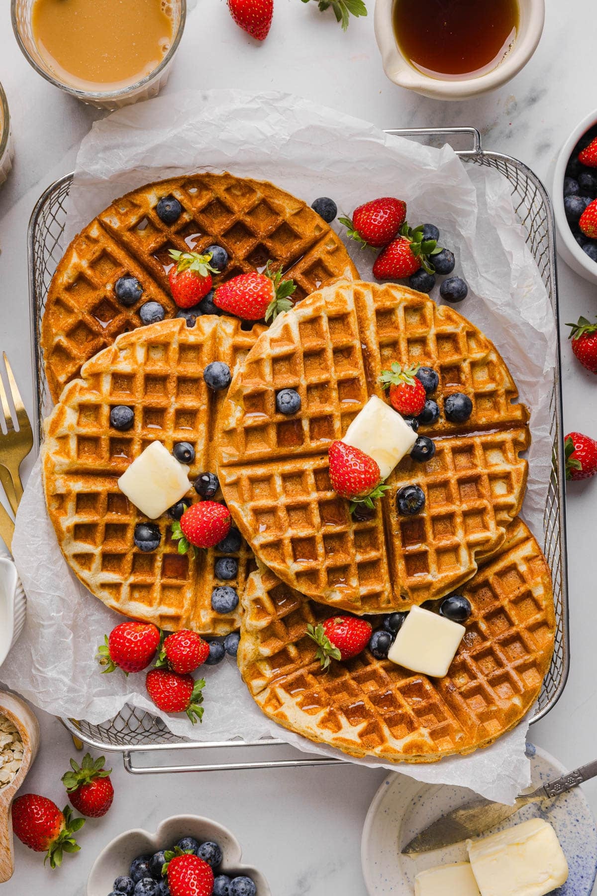 Four protein waffles with slices of butter and fresh fruit on top in a mesh serving basket.