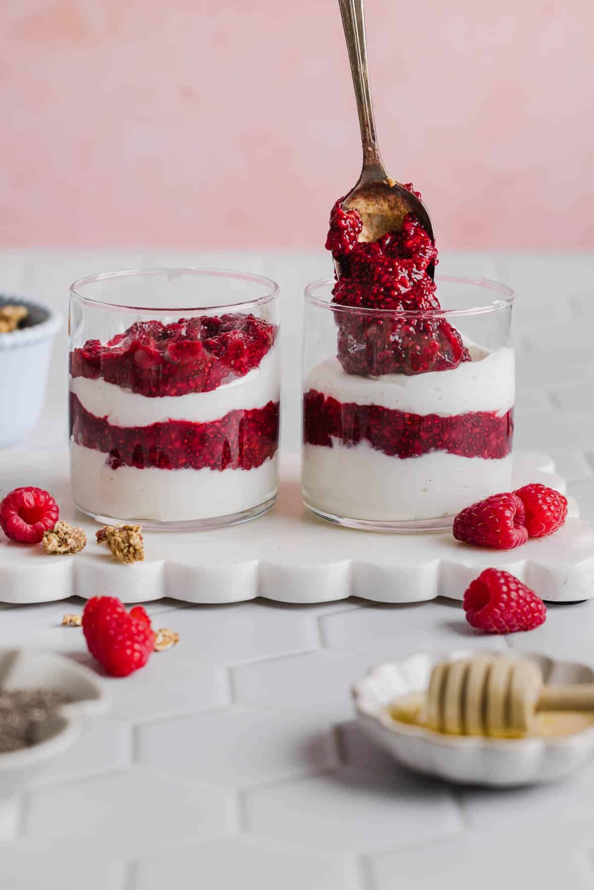 A spoon layers the yogurt and raspberry chia jam in the glasses.