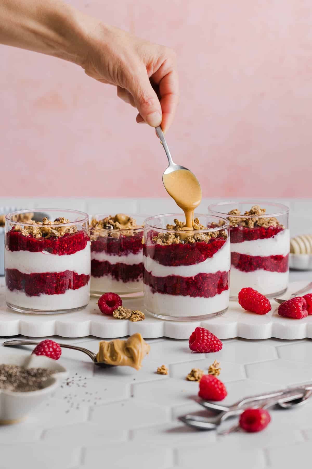 A spoon drizzles the peanut butter on top of the granola.