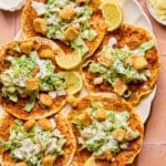 Five chicken caesar smashed tacos on a plate with lemon wedges as garnish.