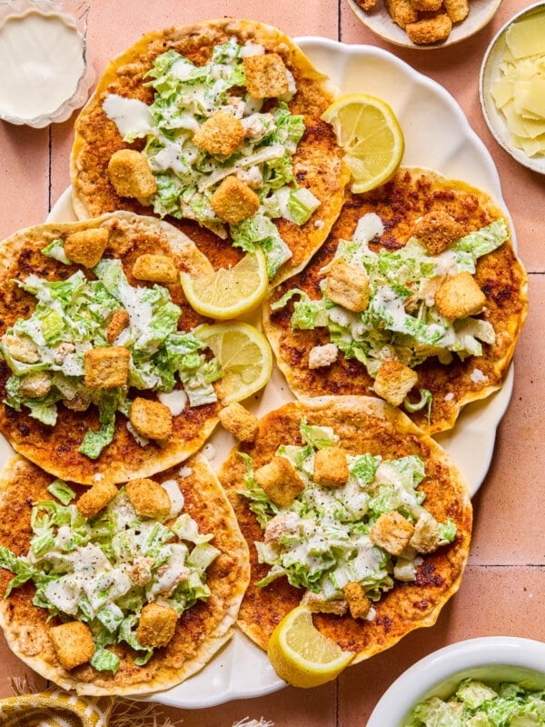 Five chicken caesar smashed tacos on a plate with lemon wedges as garnish.