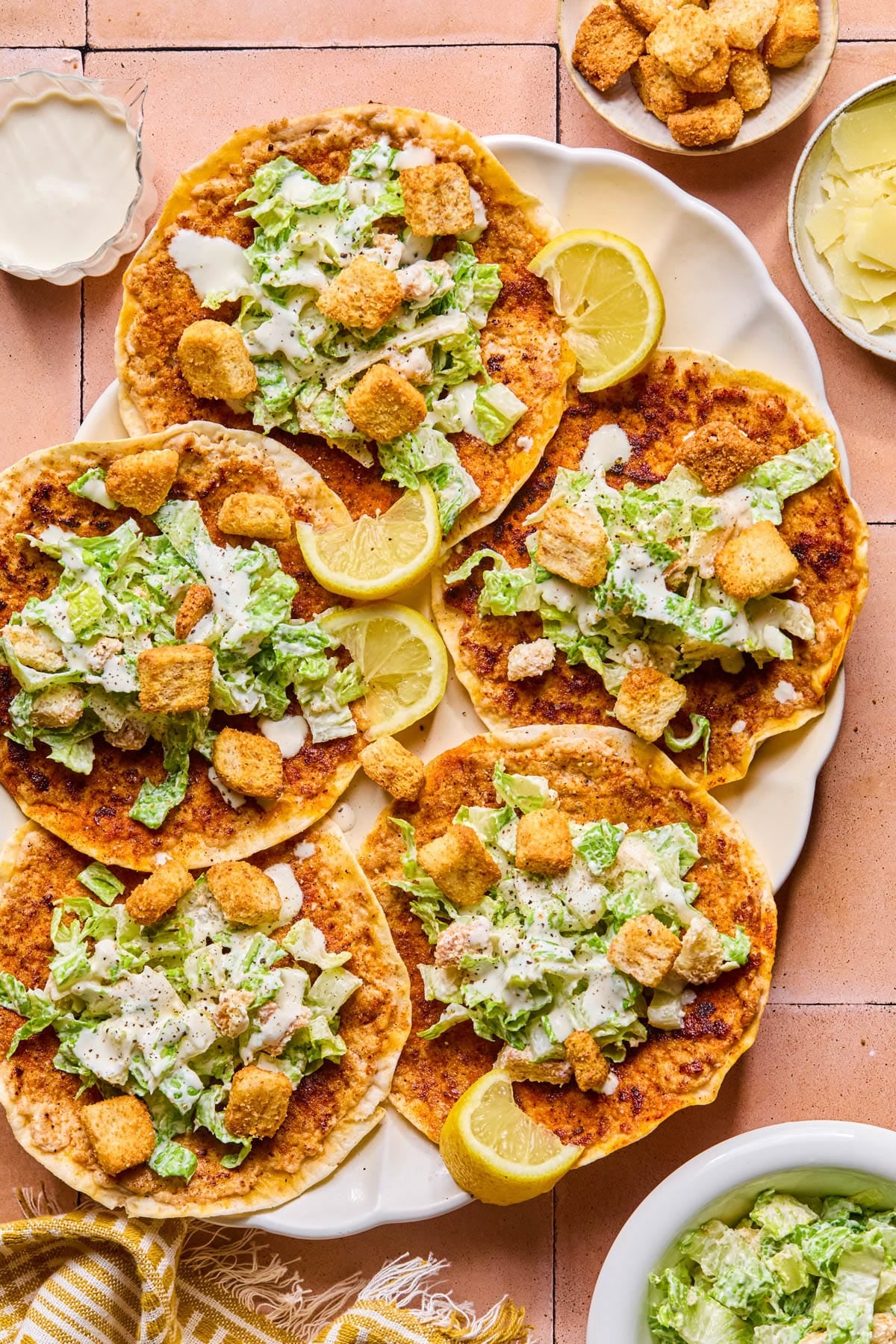 Five chicken caesar smashed tacos on a plate with lemon wedges as garnish.