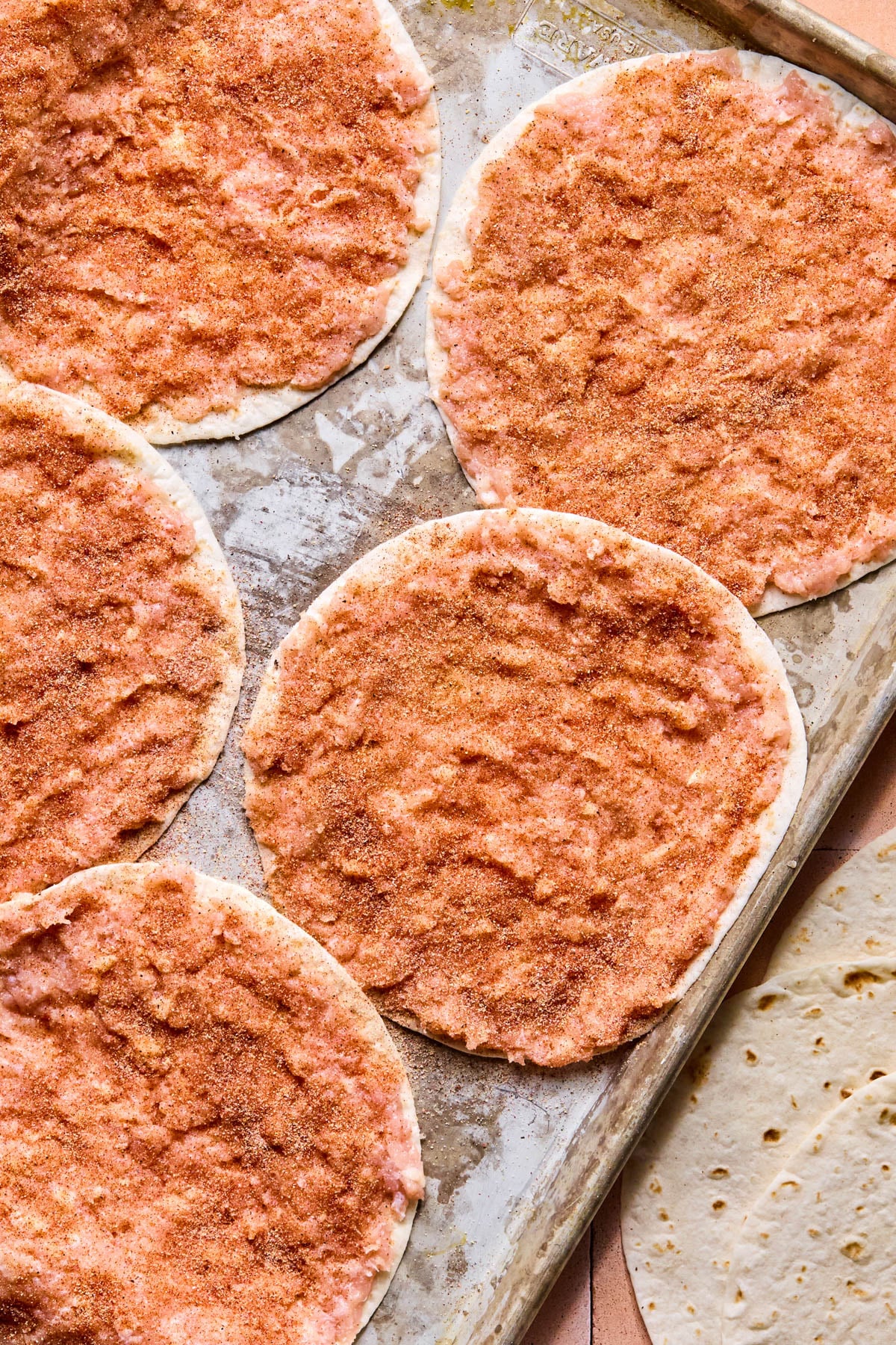 The ground chicken on the tortillas on a baking sheet with the seasonings sprinkled on top.