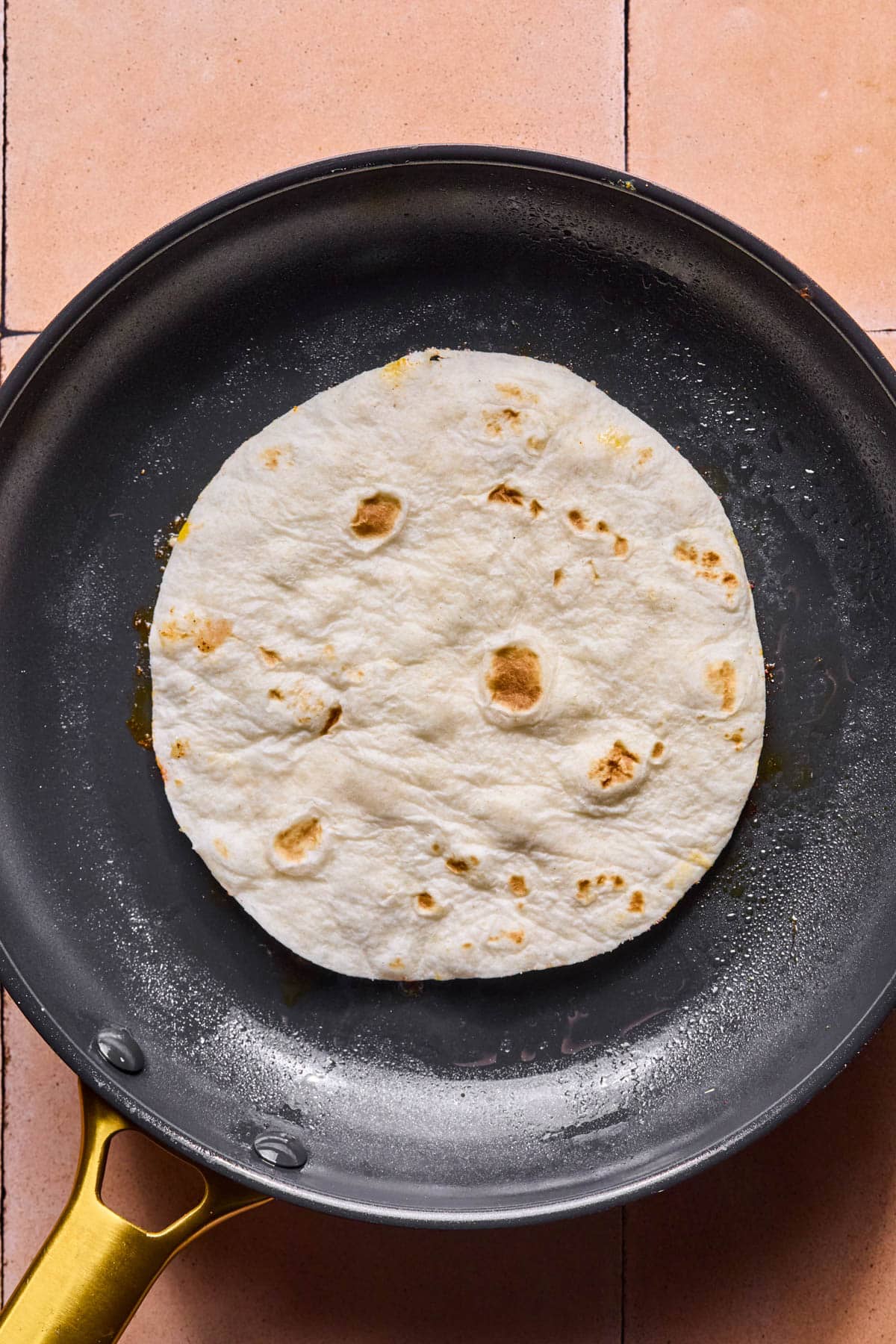 A single tortilla with the chicken side down in a hot skillet.