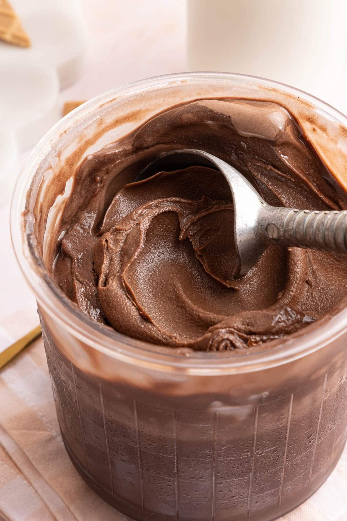 Ninja creami chocolate protein ice cream in a pint container with an ice cream scoop sitting in it.