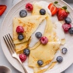 Cottage cheese crepes on a white plate with fresh blueberries, raspberries and blueberries garnished on top.