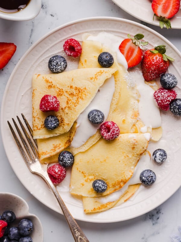 Cottage cheese crepes on a white plate with fresh blueberries, raspberries and blueberries garnished on top.