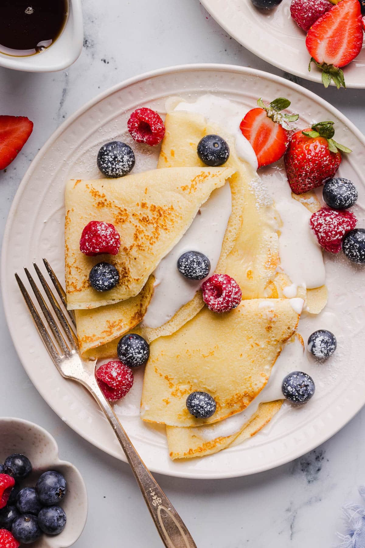 Cottage cheese crepes on a white plate with fresh blueberries, raspberries and blueberries garnished on top.