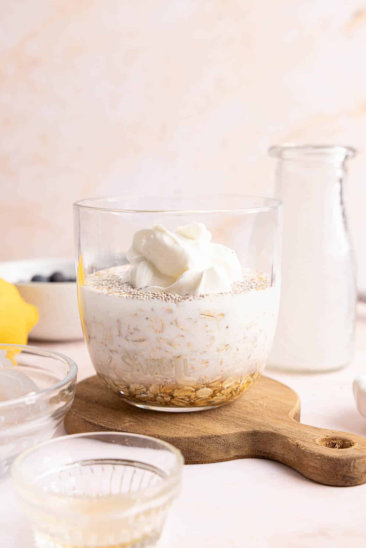 The oats, yogurt, milk, chia, vanilla, lemon zest, lemon juice, and maple syrup in a jar on a countertop.