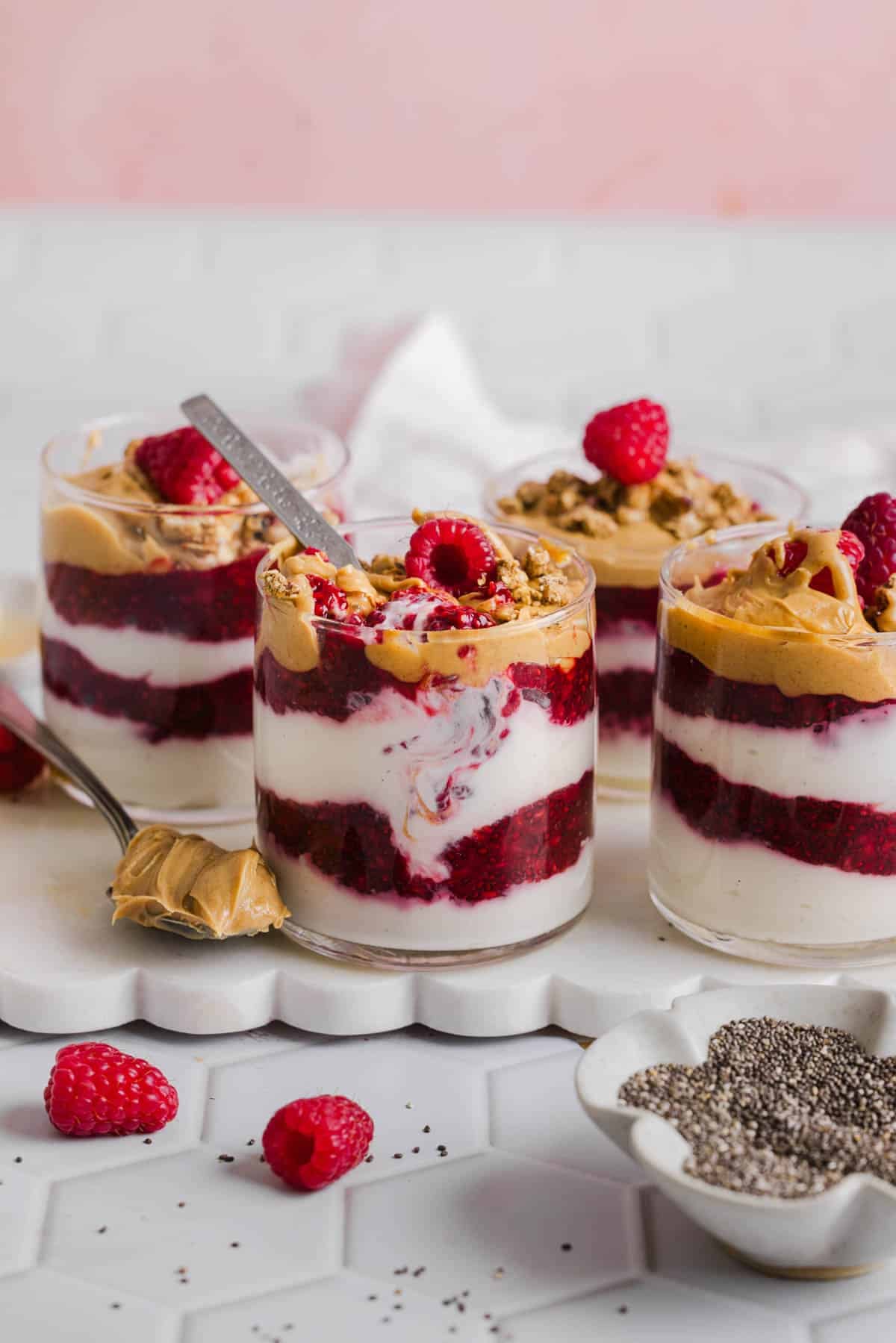 Four jars of peanut butter and jelly yogurt parfaits sit on top of a white serving platter on a white countertop.