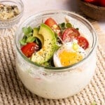 Savory overnight oats in a glass container with the savory toppings on top including sliced tomatoes, avocado, microgreens, and fried egg.