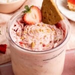 Strawberry cheesecake made in the ninja creami in the ninja creami container with a sliced strawberry and graham cracker on top.