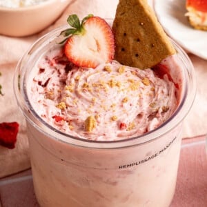 Strawberry cheesecake made in the ninja creami in the ninja creami container with a sliced strawberry and graham cracker on top.