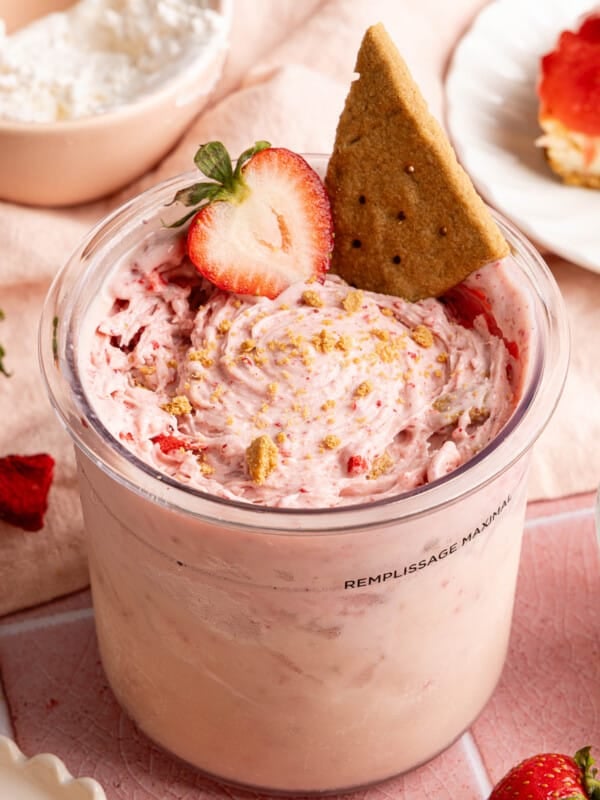 Strawberry cheesecake made in the ninja creami in the ninja creami container with a sliced strawberry and graham cracker on top.