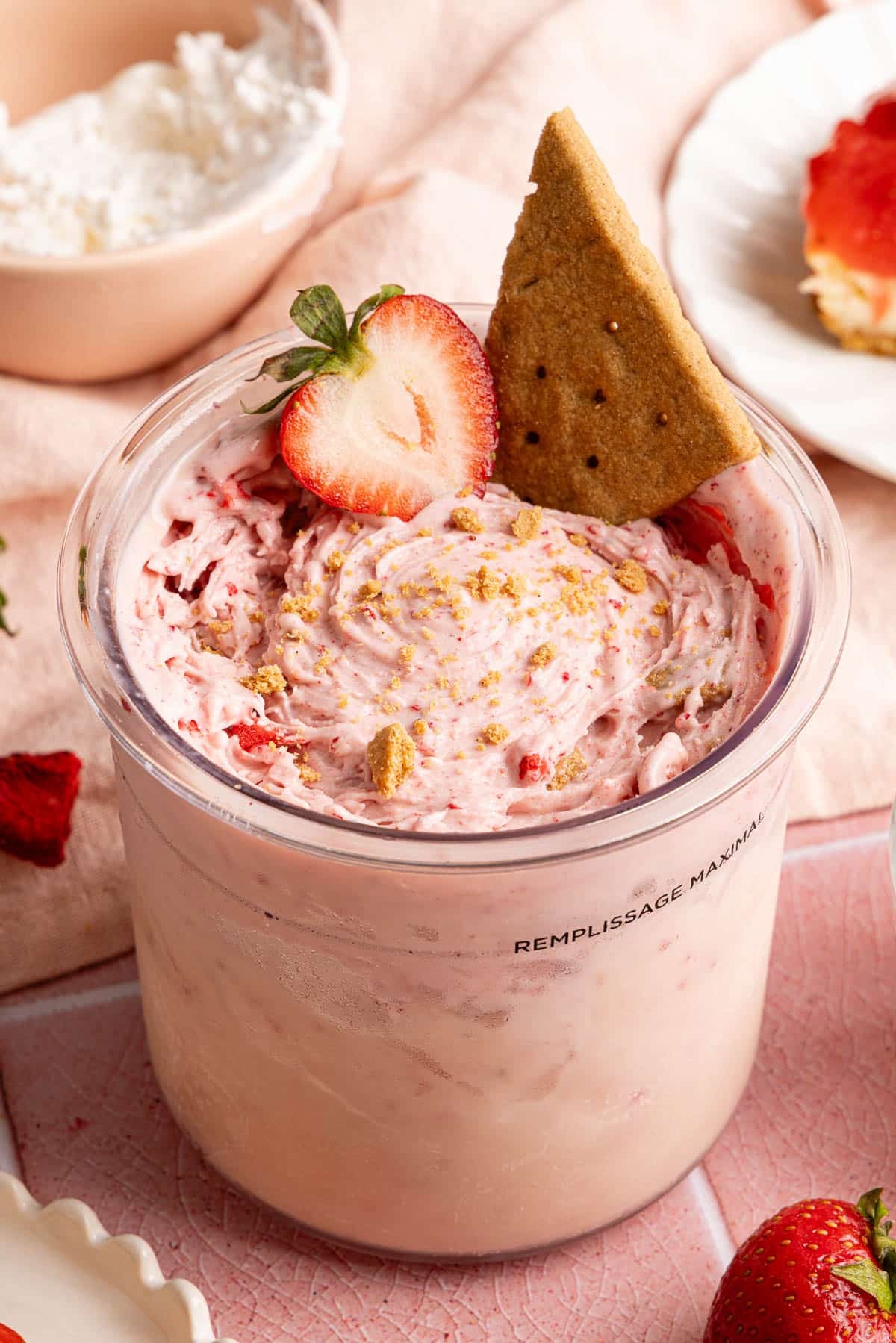 Strawberry cheesecake made in the ninja creami in the ninja creami container with a sliced strawberry and graham cracker on top.
