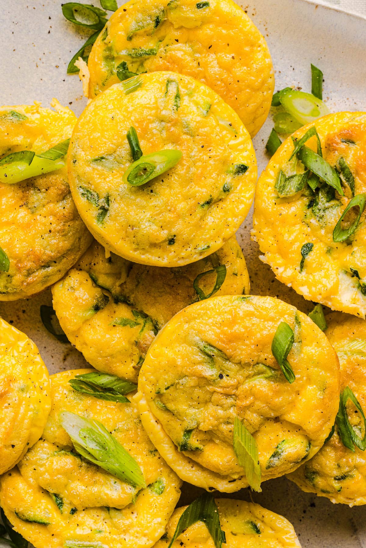 Zucchini egg muffins sitting on a white plate for serving with green onions on top for garnish.