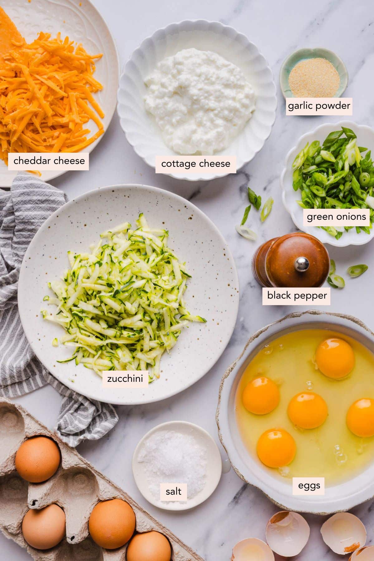 All of the ingredients for zucchini egg muffins in bowls on a countertop.