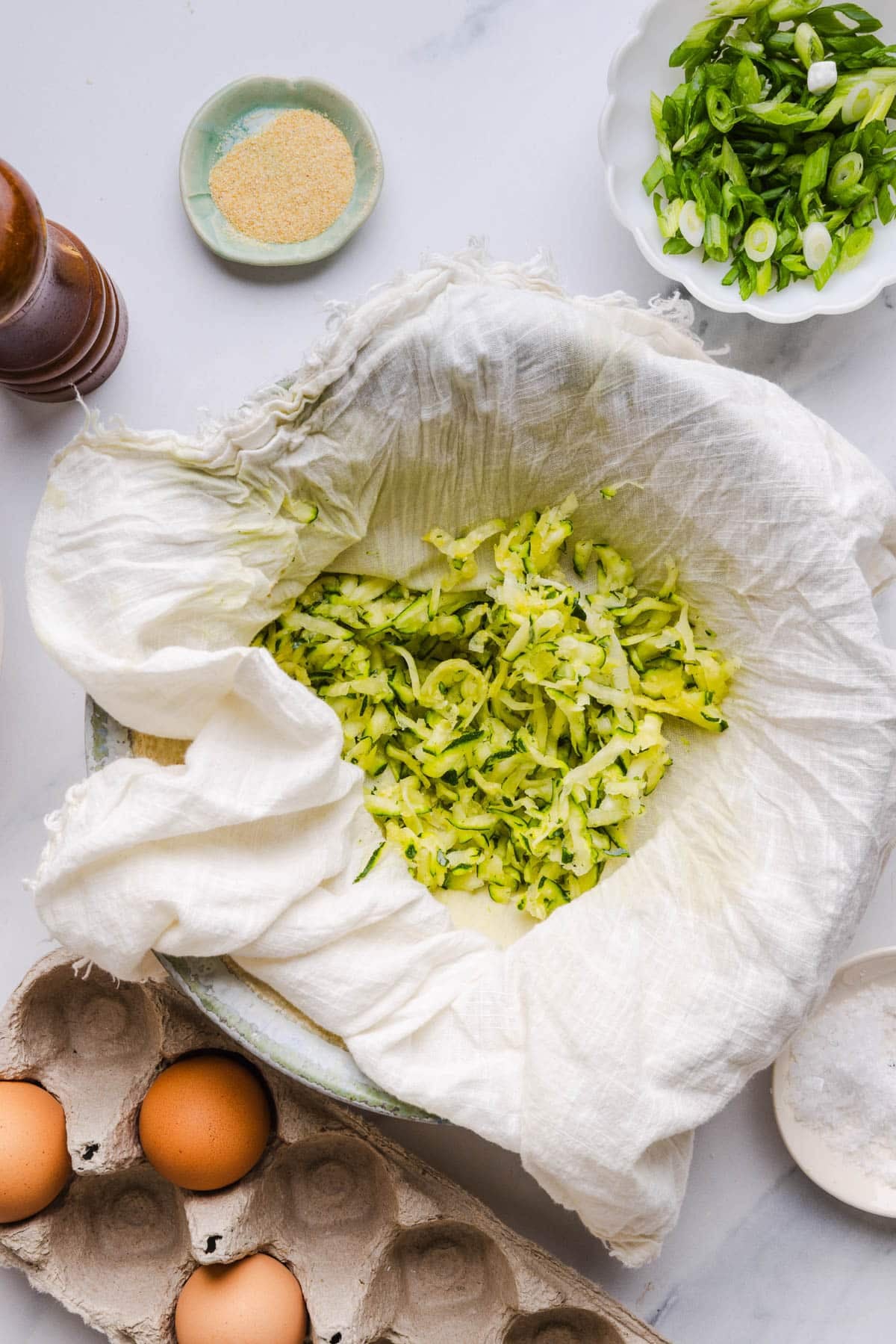 The shredded zucchini on a clean kitchen towel in a bowl.