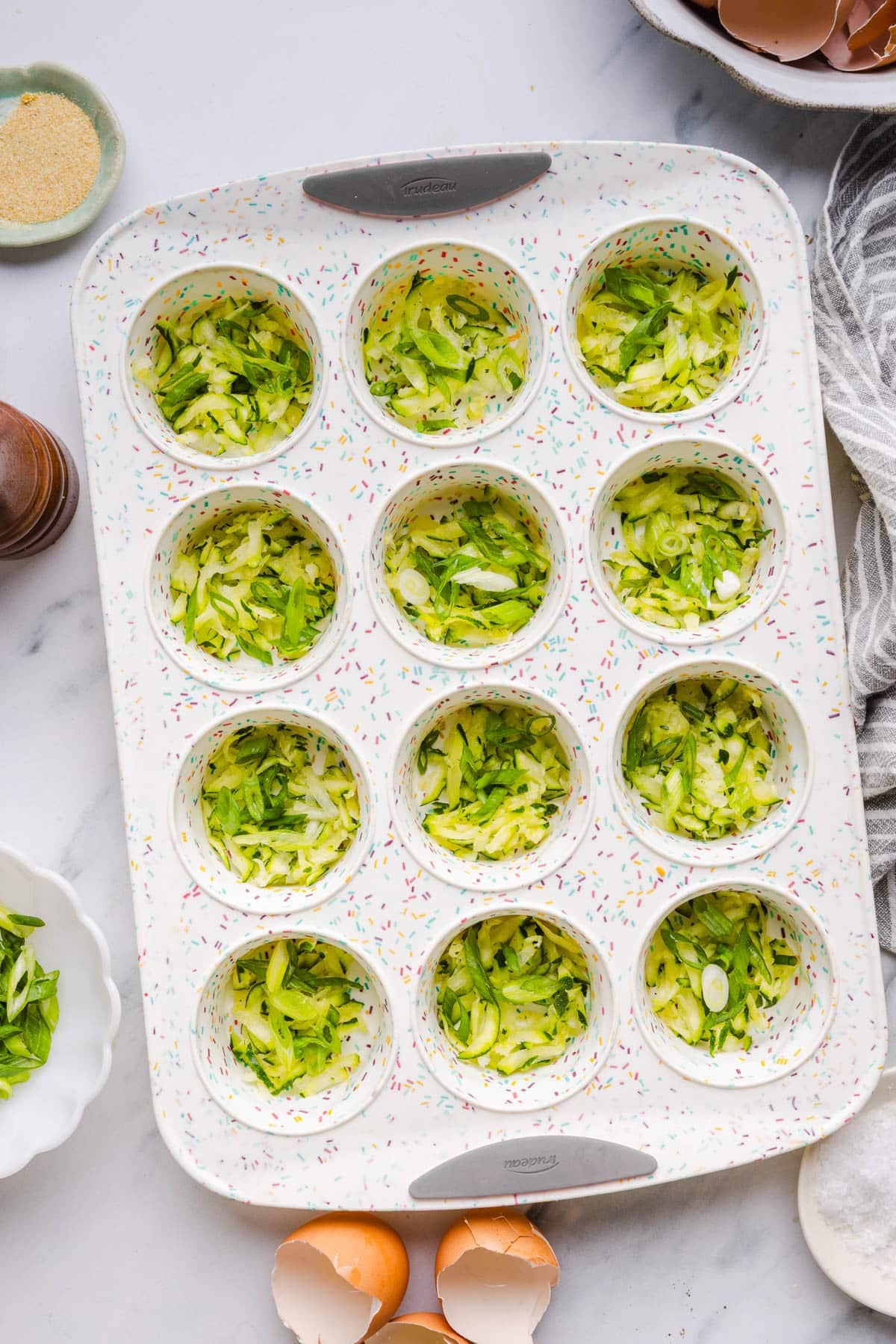 The zucchini and green onions in the bottom of the muffin pan tins.