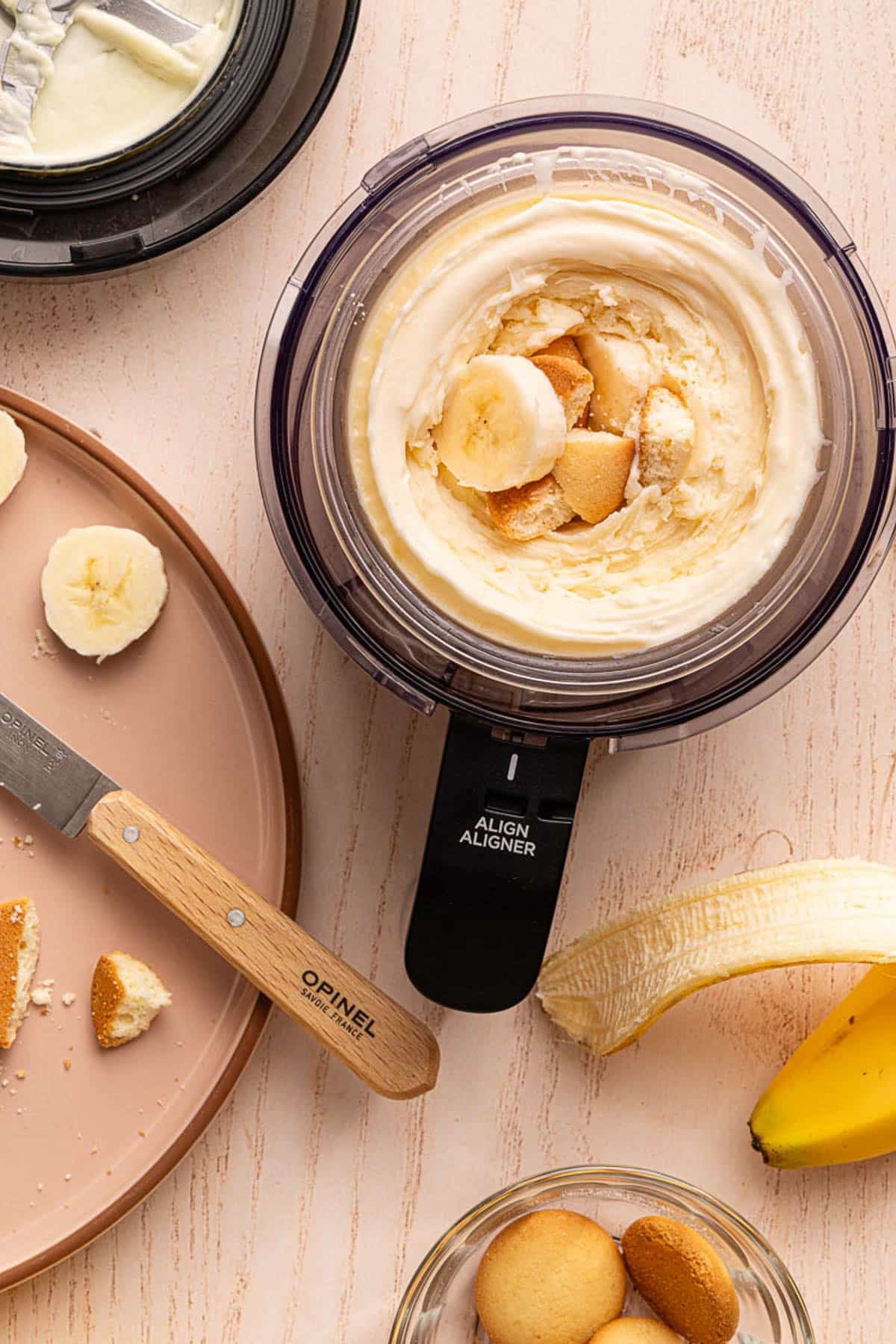 Cut bananas and broken nilla wafers rest in the hole in the middle of the ice cream in the container.