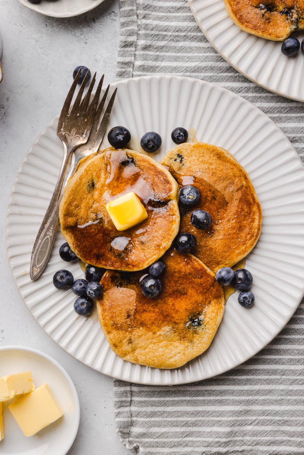 Three blueberry cottage cheese pancakes on a white plate with a slice of butter and fresh blueberries.