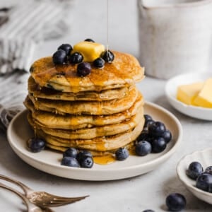A stack of blueberry pancakes on a white plate with fresh blueberries.