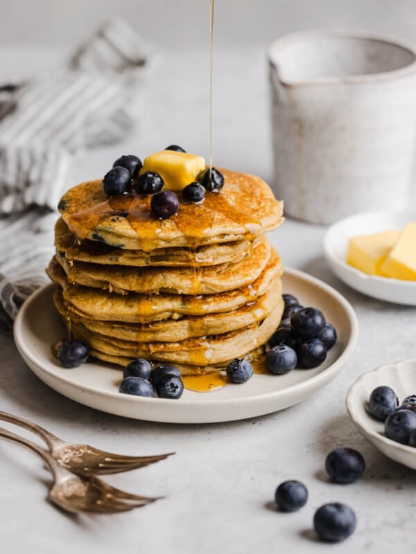 A stack of blueberry pancakes on a white plate with fresh blueberries.