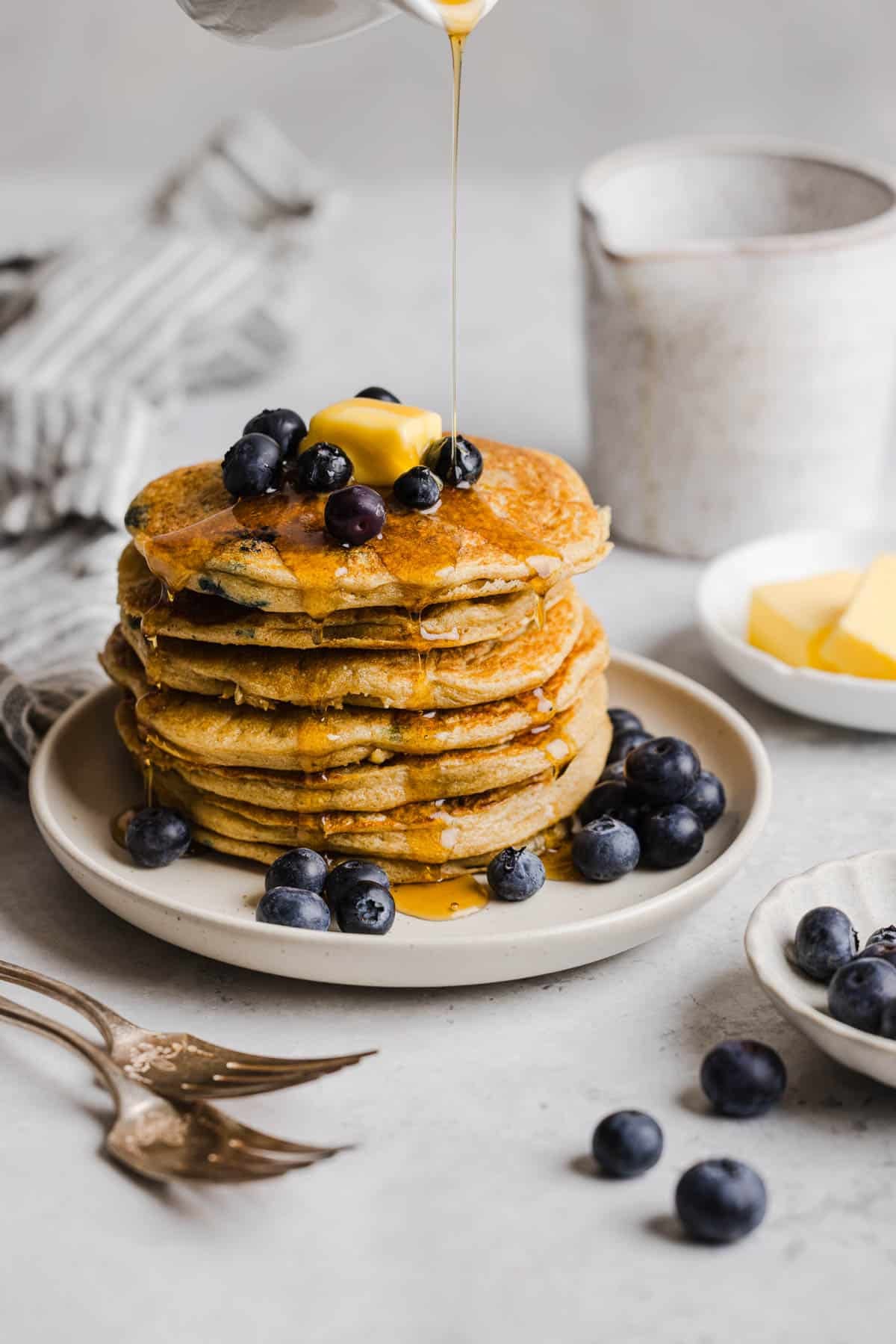 A stack of blueberry pancakes on a white plate with fresh blueberries.