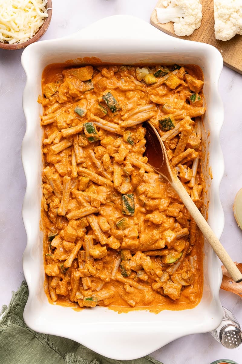 The cooked pasta, pasta sauce, and veggies mixed together in a white rectangular dish.