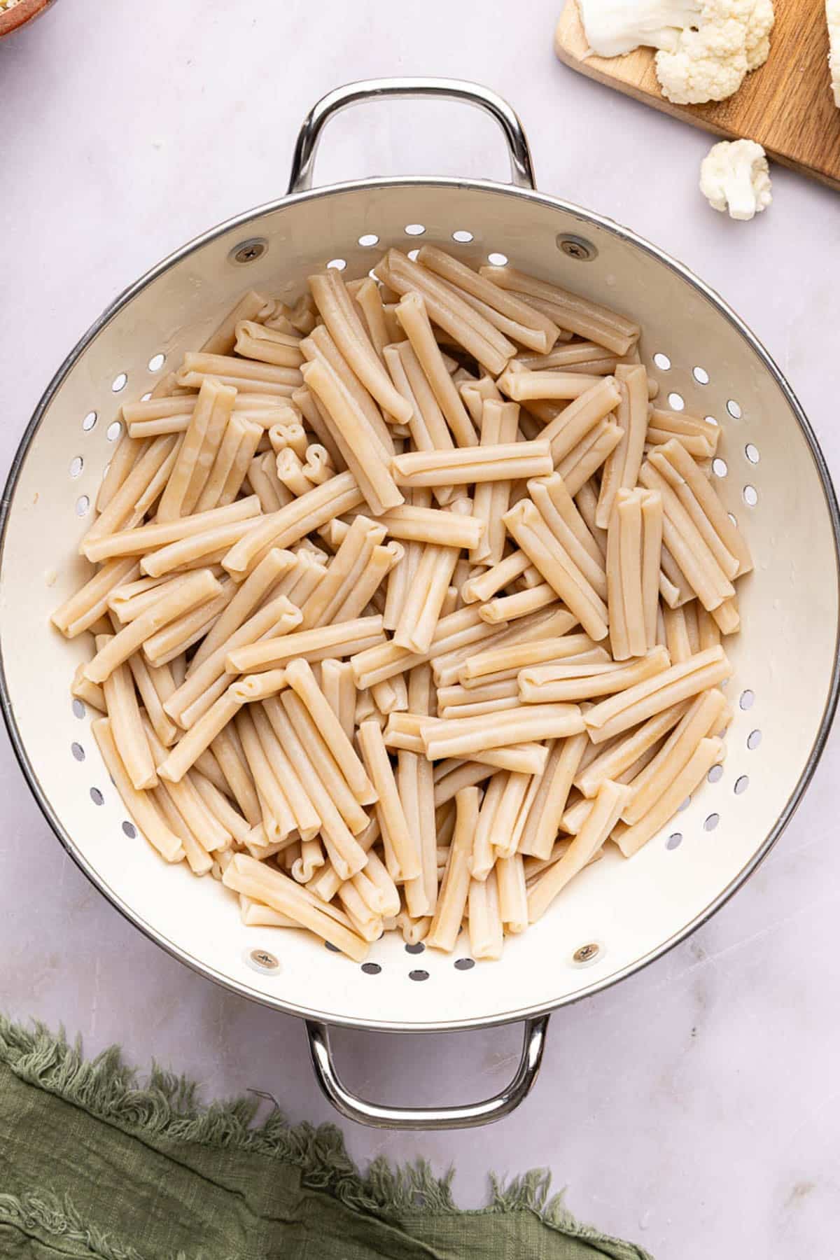 The drained pasta in a pasta strainer on a countertop.