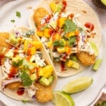 Two fish stick tacos on a white plate with lime wedges on the side for garnish.