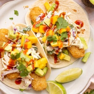 Two fish stick tacos on a white plate with lime wedges on the side for garnish.