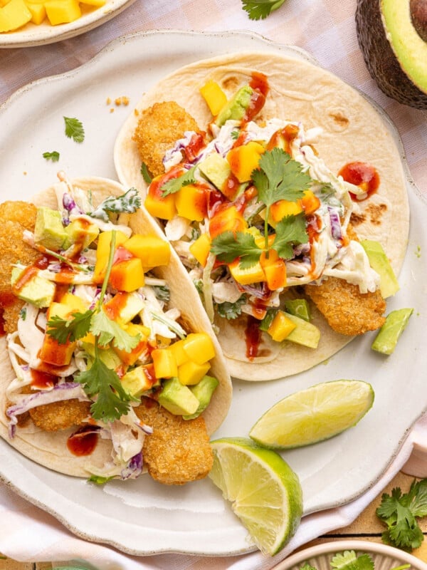 Two fish stick tacos on a white plate with lime wedges on the side for garnish.