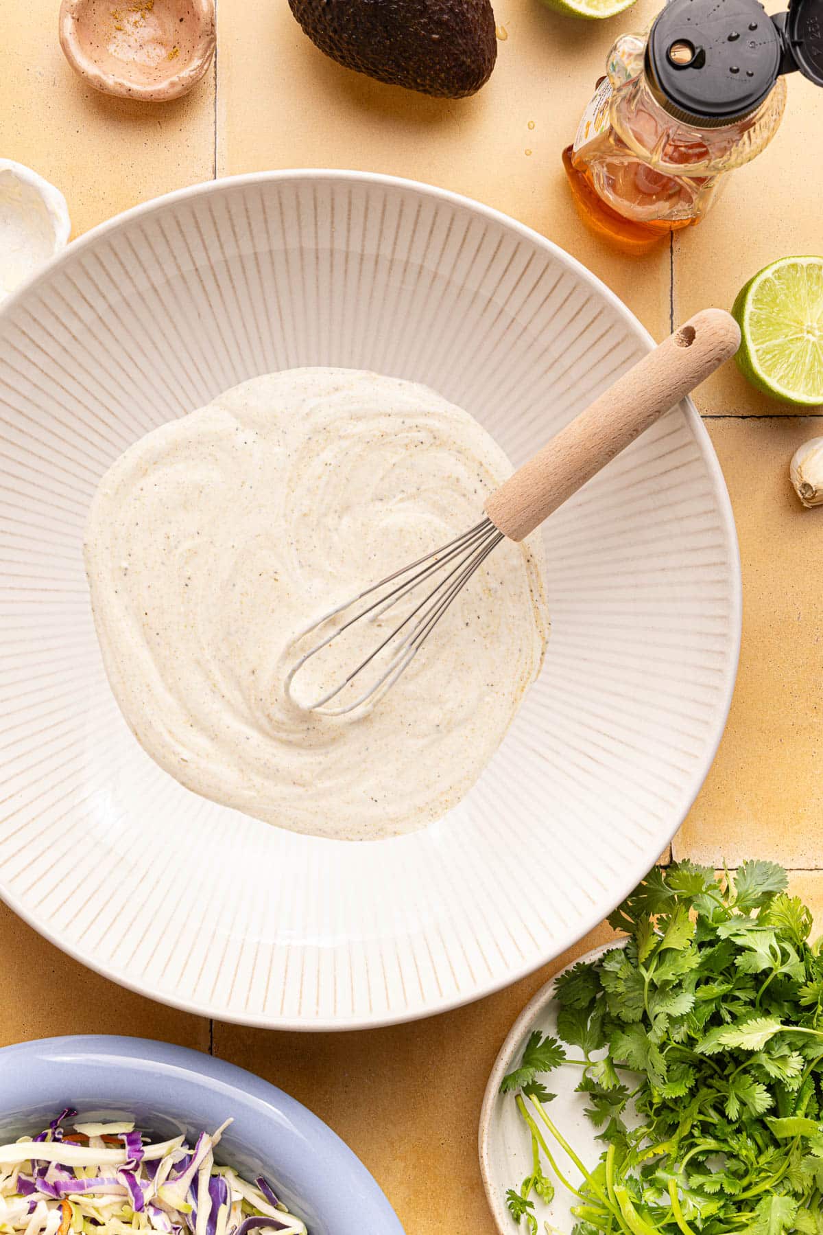 The slaw dressing in a white bowl with a whisk.