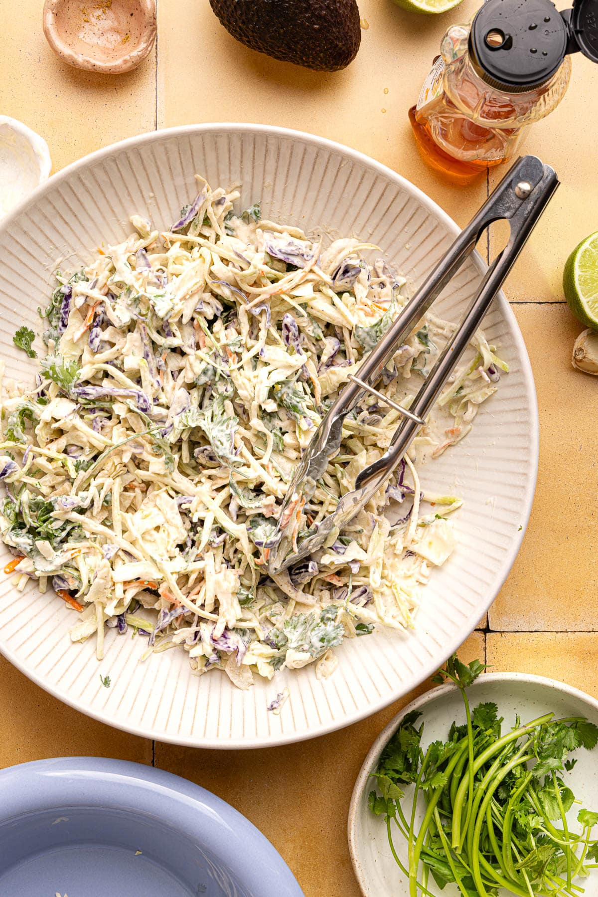 The slaw mixed together in a while bowl with serving tongs.