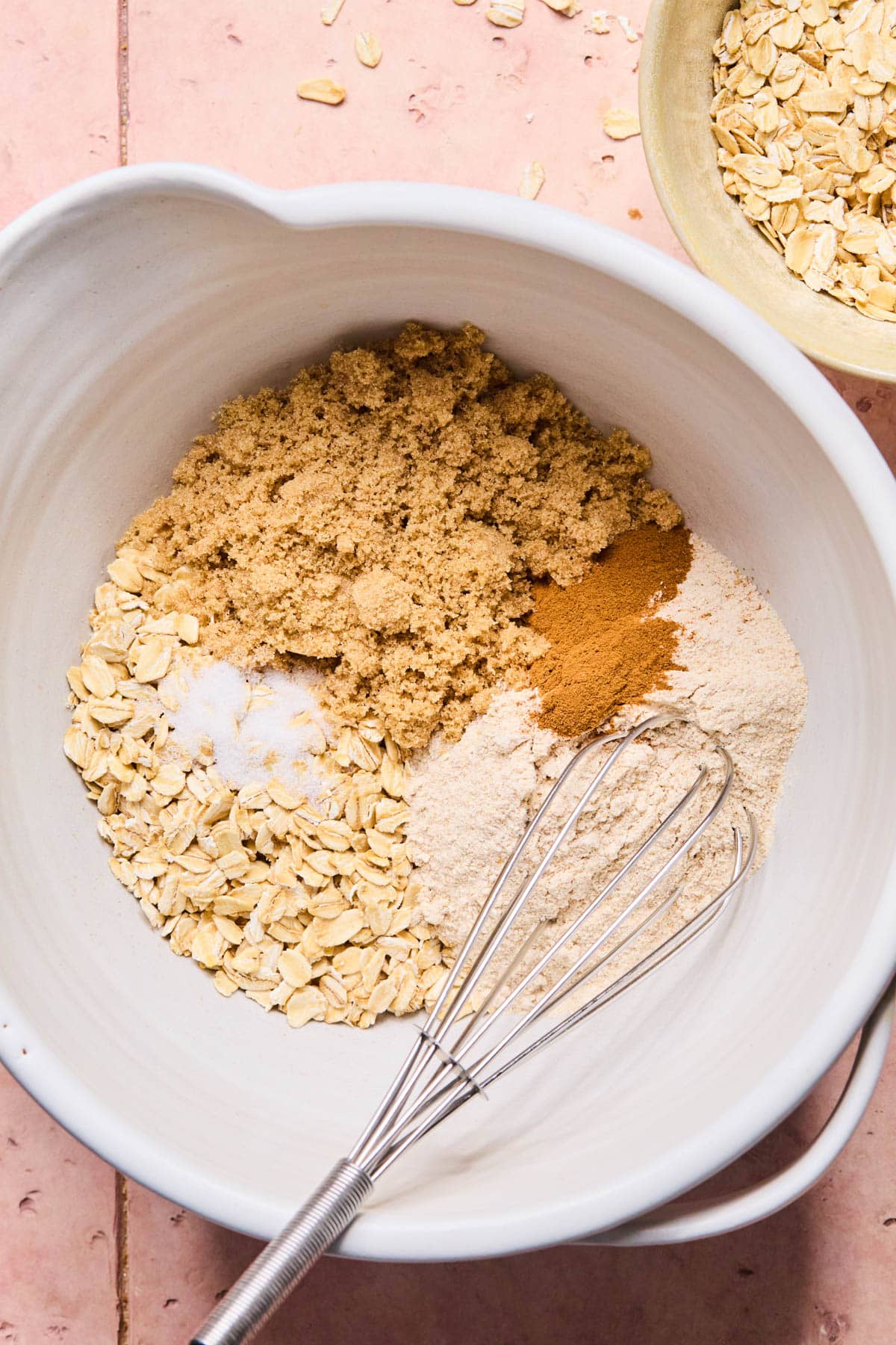 The flour, oats, sugar, salt, and cinnamon in a white bowl before whisking.