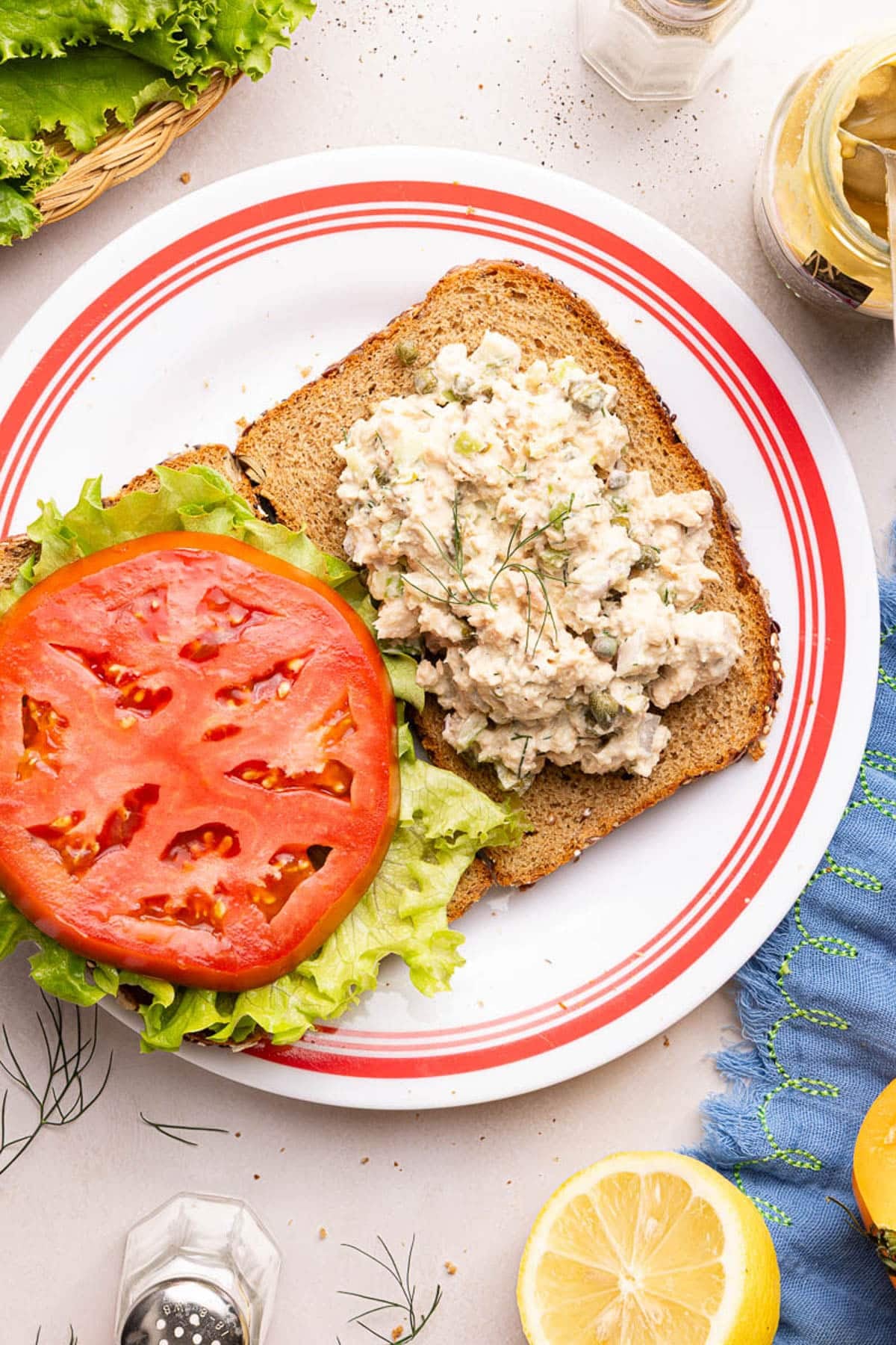 A slice of bread with salmon salad on top next to another slice of bread with lettuce and tomato on top.