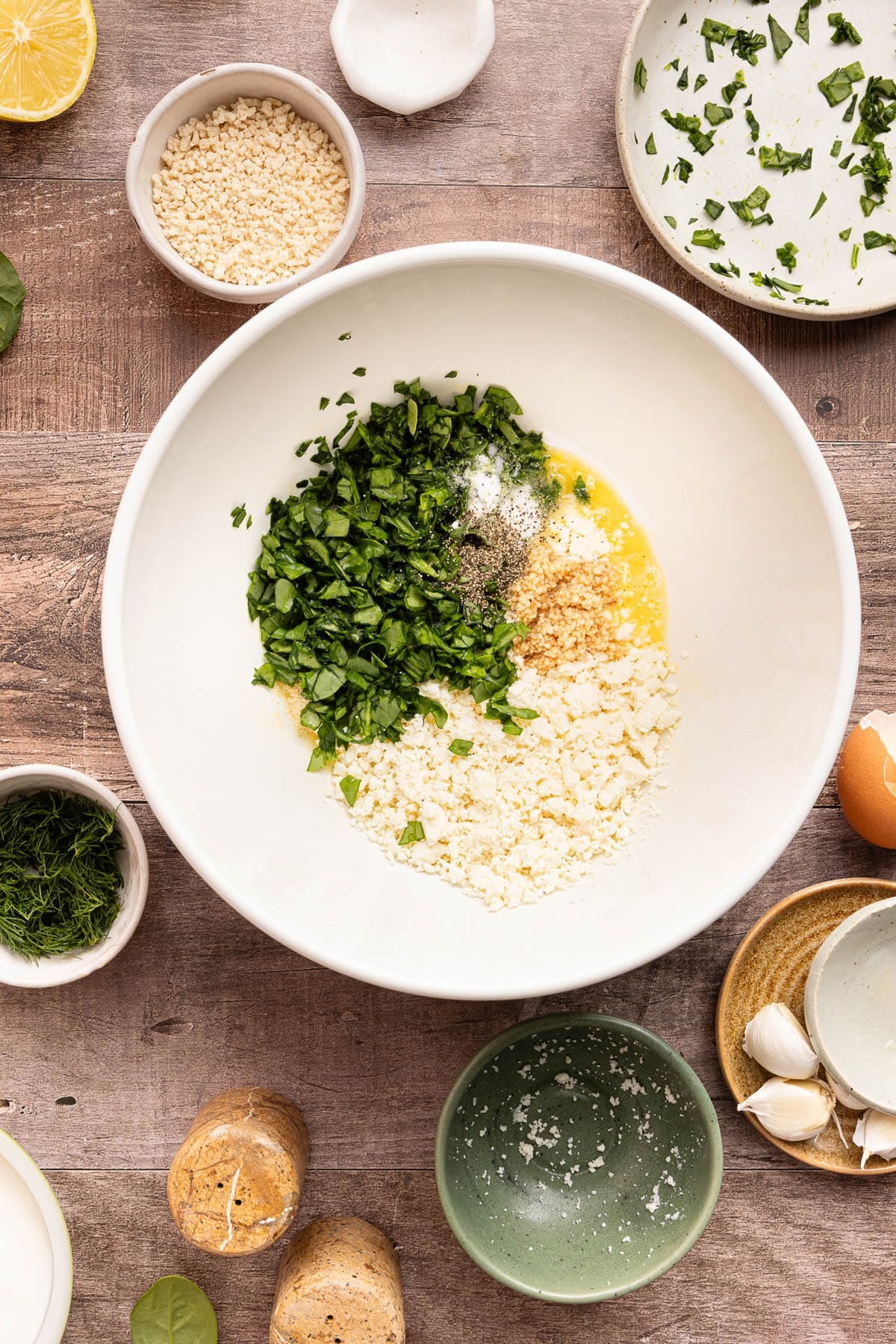 A white bowl with egg, feta, breadcrumbs, garlic, spinach, onion powder, salt and pepper before stirring.
