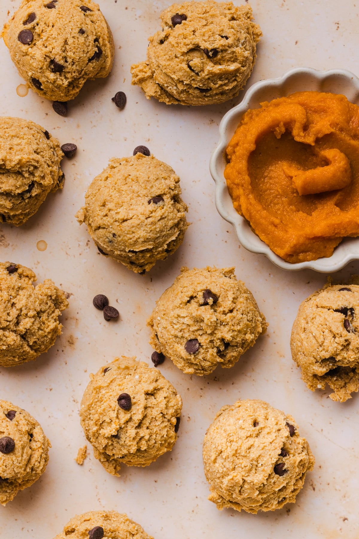 Edible pumpkin cookie dough balls on a countertop with a bowl of extra canned pumpkin on the side.