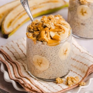 Peanut butter banana chia pudding in a glass on a napkin on a countertop.
