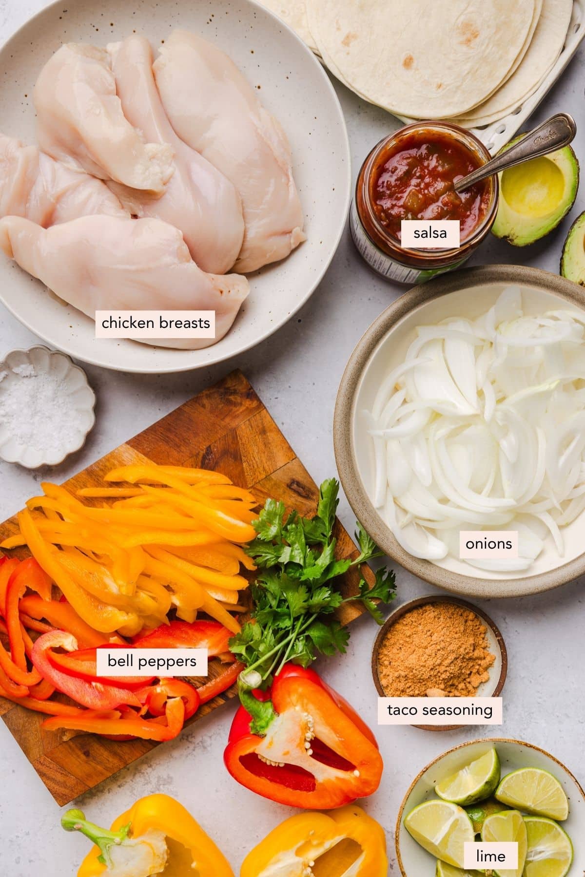 All of the ingredients for slow cooker chicken fajitas in bowls or cutting board on a countertop.