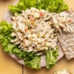 Honey mustard chicken salad on a plate served over lettuce with a cracker on the side.