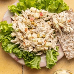 Honey mustard chicken salad on a plate served over lettuce with a cracker on the side.