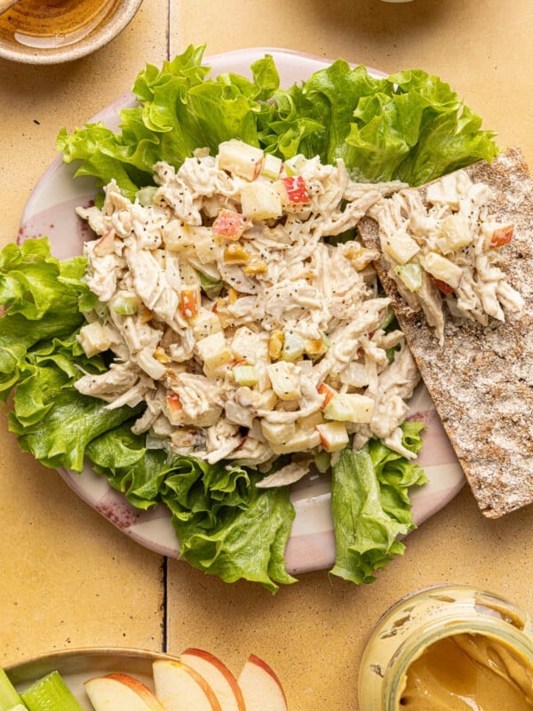 Honey mustard chicken salad on a plate served over lettuce with a cracker on the side.