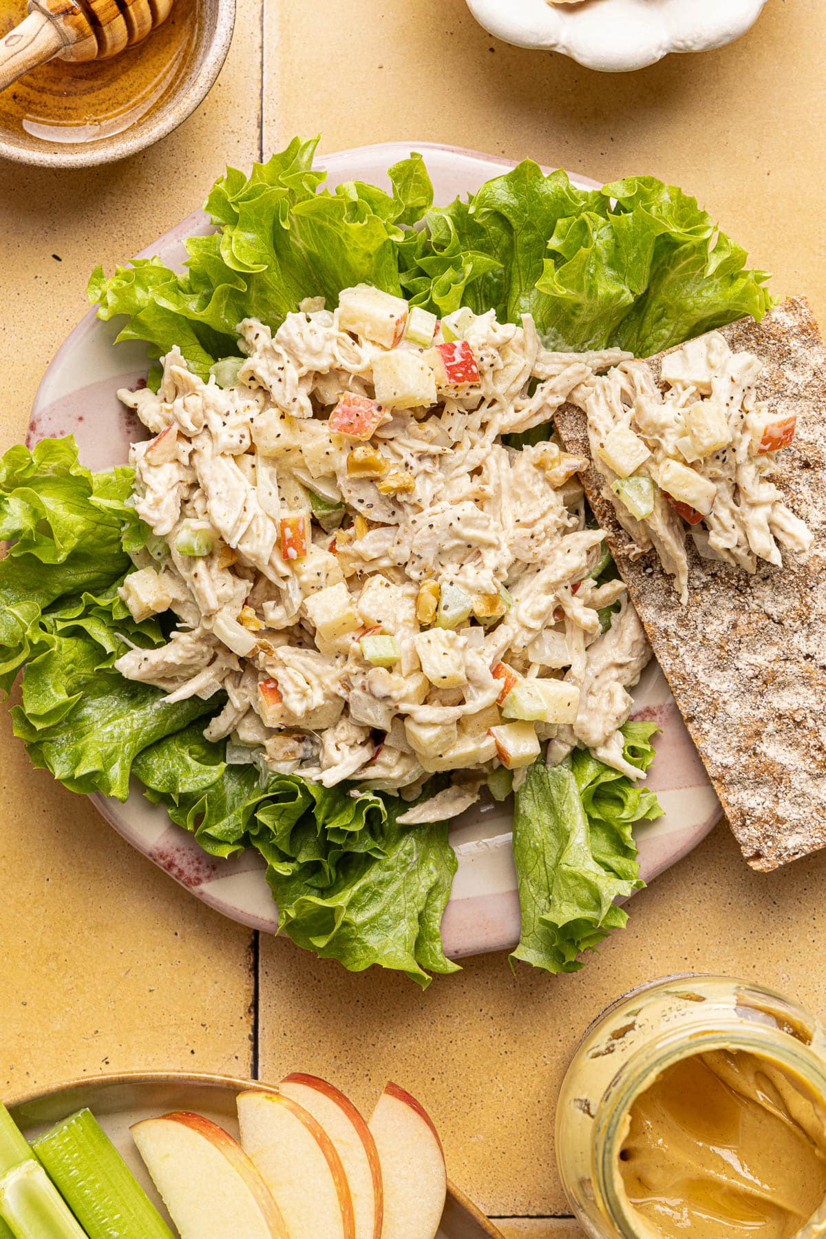 Honey mustard chicken salad on a plate served over lettuce with a cracker on the side.