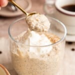 A spoon lifts coffee overnight oats from a glass sitting on a countertop.