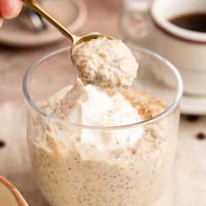 A spoon lifts coffee overnight oats from a glass sitting on a countertop.