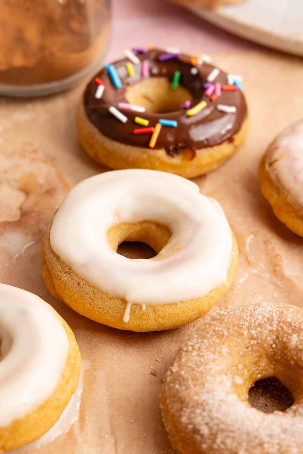 The frosted donuts sitting on a piece of parchment paper.