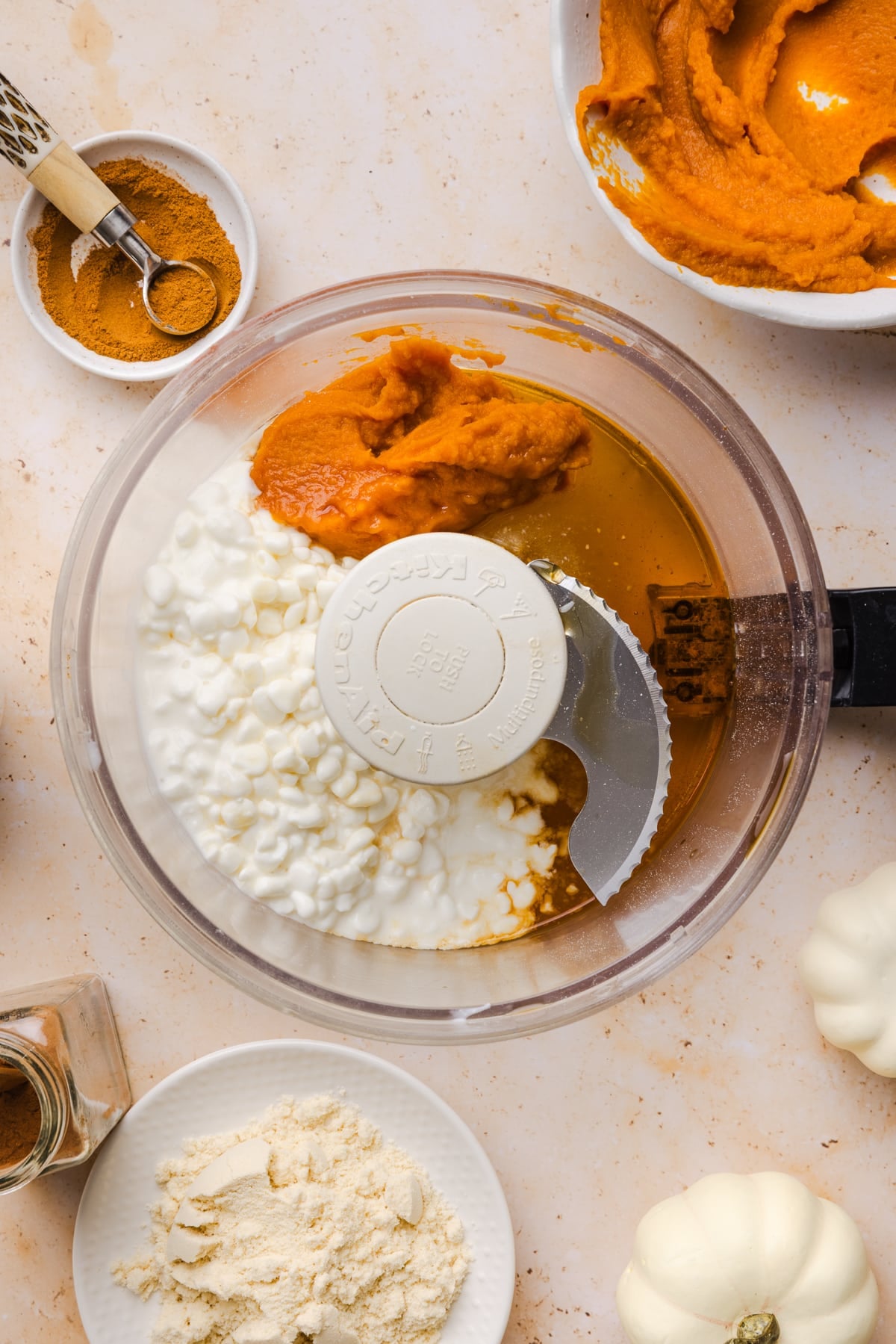 The cottage cheese, pumpkin, maple syrup, and vanilla extract in the bowl of a food processor before blending.