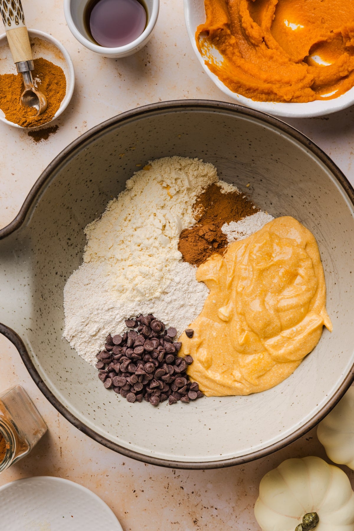 The blended cottage cheese pumpkin mixture in a bowl with the protein powder, oat flour, spices, and chocolate chips before mixing.